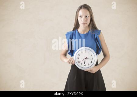 Giovane donna che tiene un orologio davanti alla pancia. Concetto di orologio biologico Foto Stock