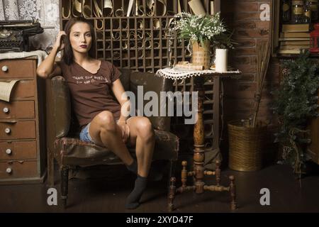 Una giovane donna siede su una poltrona sullo sfondo di interni vintage Foto Stock