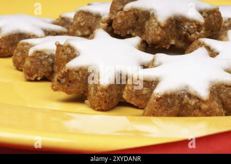 Primo piano di alcuni biscotti alle stelle della cannella (in tedesco Zimtsterne), tipici biscotti di Natale tedeschi e svizzeri su un piatto giallo su sfondo rosso Foto Stock