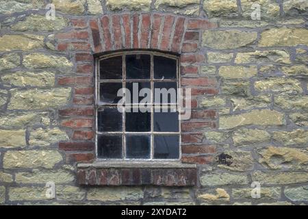 Singola finestra incastonata in un muro in pietra in muratura con struttura in mattoni in una vecchia fattoria, Renania settentrionale-Vestfalia, Germania, Europa Foto Stock