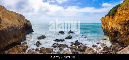 Vista panoramica di una splendida insenatura rocciosa e della costa con onde che si infrangono contro le scogliere sotto un cielo azzurro soleggiato con nuvole sparse. portogallo Foto Stock
