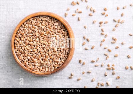 Chicchi di frumento tenero, pane di frumento in una ciotola di legno su tessuto di lino. Triticum aestivum, un'erba ampiamente coltivata per i suoi semi, un cereale. Foto Stock