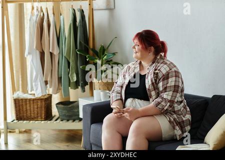 Una bella donna di grandi dimensioni si rilassa sul divano di casa, tenendo un telefono. Foto Stock