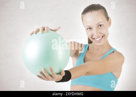 Montare donna in piedi e in possesso di una sfera di pilates, isolato in grigio Foto Stock