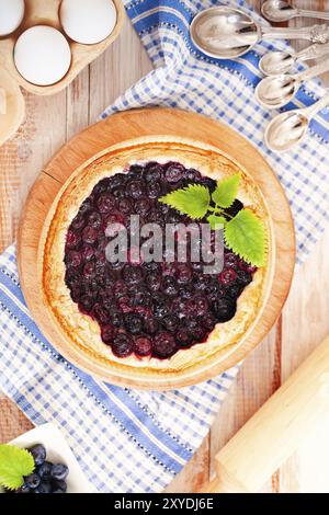 Vista dall'alto della deliziosa crostata aromatica fatta in casa con mirtilli guarniti con foglie di menta verde poste su un tovagliolo su un tavolo di legno con ingredienti e u Foto Stock