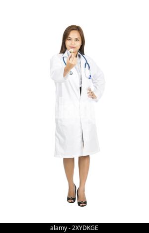 Una bella donna asiatica che indossa un camice da laboratorio bianco e uno stetoscopio, una calda espressione sorridente, un braccio akimbo che mostra una sigaretta rotta davanti a te Foto Stock