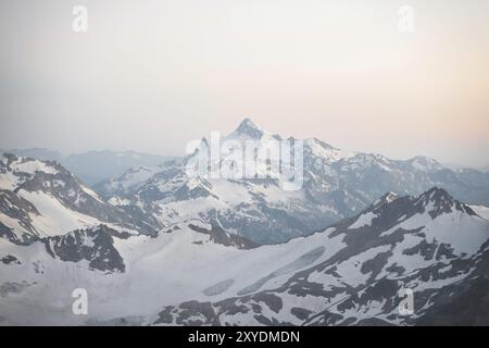 Un panorama al tramonto dell'elbrus e parte della cresta caucasica con nuvole arancioni e un ghiacciaio incrinato sul fondo Foto Stock