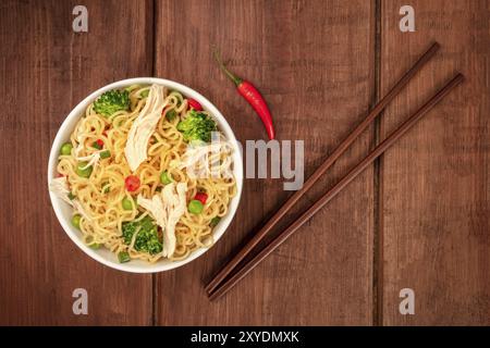 Soba Noodles con verdure e carne di pollo, girato dalla parte superiore al buio su un rustico sfondo di legno con bacchette Foto Stock