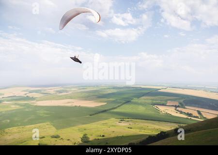 Un parapendio bianco-arancio vola sul terreno montuoso Foto Stock