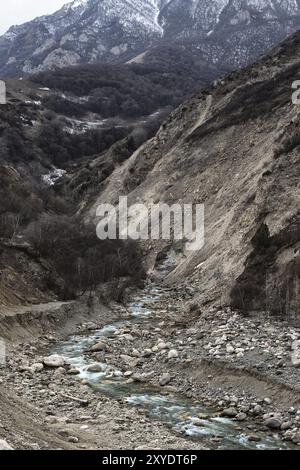 Un veloce fiume di montagna scorre lungo i pendii rocciosi delle montagne grigie del Caucaso nel periodo autunnale invernale Foto Stock