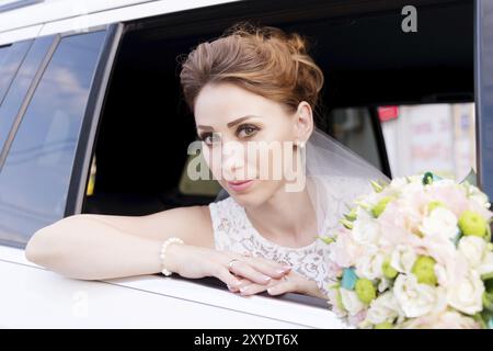 Ritratto ravvicinato di una splendida sposa accanto al suo bouquet di nozze nella finestra di una macchina da sposa. Il concetto di grazia nuziale Foto Stock