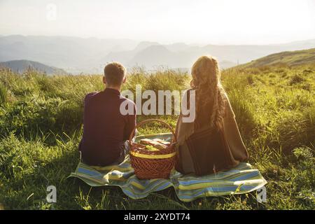 Vista dal retro. Giovane coppia di sposi in un picnic all'aperto al tramonto. Il concetto di una giovane famiglia felice e di unità con la natura Foto Stock