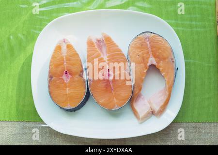 Tre bistecche di salmone fresco su un piatto bianco in piedi su un tavolo verde. Vista dall'alto Foto Stock