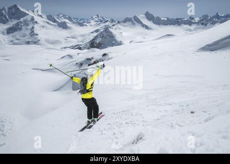 Uno sciatore con attrezzatura sportiva completa salta nell'abisso dalla cima del ghiacciaio sullo sfondo del cielo blu e del Caucaso innevato Foto Stock