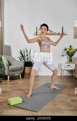 Una giovane donna con un top di raccolto esegue una posa yoga su un tappeto in un appartamento moderno. Foto Stock