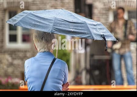 Un cittadino anziano siede sotto un ombrello Foto Stock