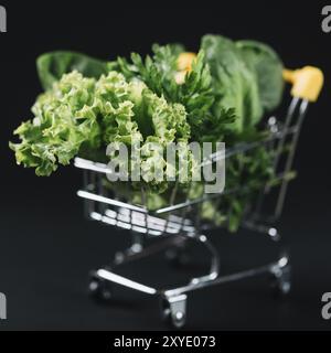 Primo piano, carrello della spesa con verdure a foglia verde, sfondo nero Foto Stock