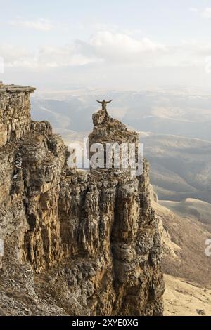 Un uomo felice con le mani in alto si erge in cima a una roccia separata che si trova sopra le nuvole sullo sfondo di valli, colline, soli Foto Stock