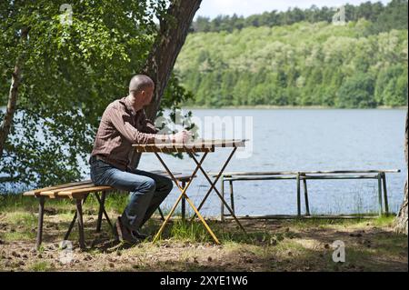 Giovane seduto sulla riva di un lago nella foresta Foto Stock