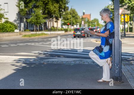 Anziano che si appoggia contro un lampione e legge un giornale Foto Stock