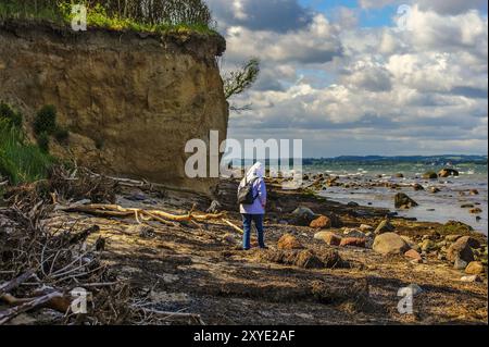 Una donna cammina sulla spiaggia sotto le scogliere Foto Stock