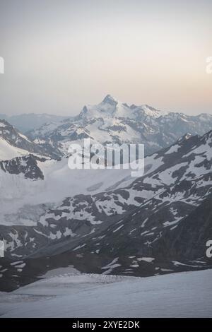 Un panorama al tramonto dell'elbrus e parte della cresta caucasica con nuvole arancioni e un ghiacciaio incrinato sul fondo Foto Stock