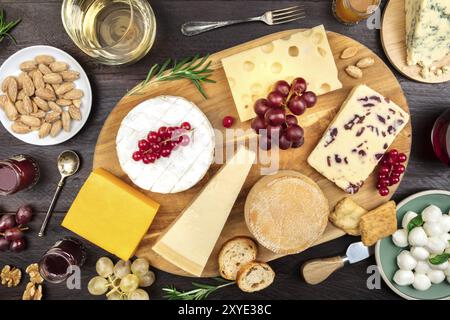 Un assortimento di vari tipi di formaggio con vino e uva, girato da sopra al buio su un sfondo rustico Foto Stock