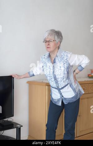 Un cittadino anziano soffre di mal di schiena e si appoggia alla televisione Foto Stock