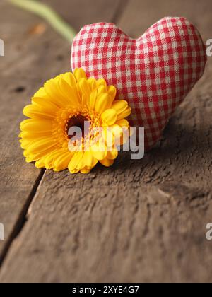 Tessuto a scacchi forma di cuore con una gerbera gialla daisy su una tavola in legno rustico, il giorno di San Valentino o la festa della mamma concetto sfondo con spazio per tex Foto Stock