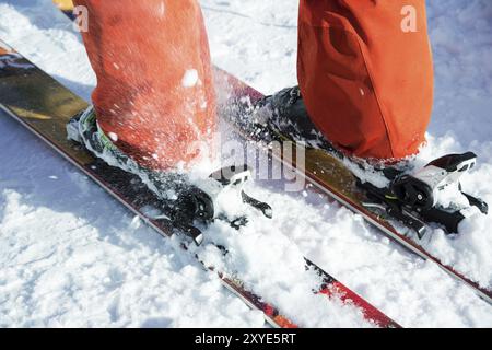 Scarponi da sci alpino arancioni in un supporto da sci. Una scarpa è completamente fissata sugli sci, la seconda no. Primo piano. Tuta arancione Foto Stock