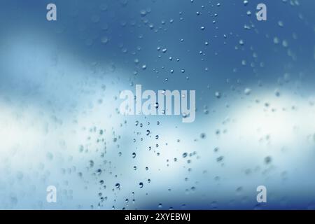 Immagine ravvicinata delle gocce d'acqua sulla finestra. Cielo blu e nuvole sullo sfondo Foto Stock