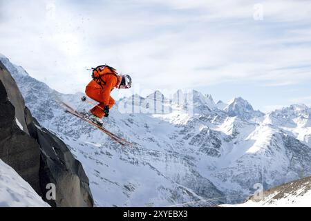 Uno sciatore professionista fa un salto da un'alta scogliera contro il cielo blu lasciando una scia di neve in montagna. Cresta caucasica nel Foto Stock