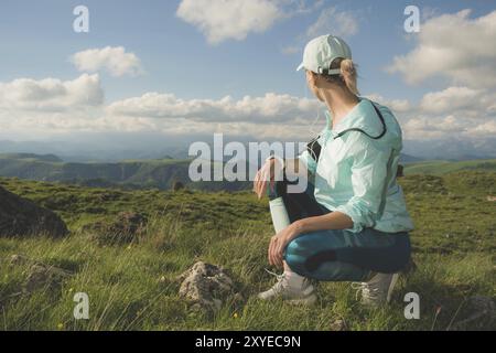 Una ragazza carina con le cuffie che si prepara a correre in un campus naturale. Riposati dopo e prima di correre. Il concetto di sport in natura Foto Stock