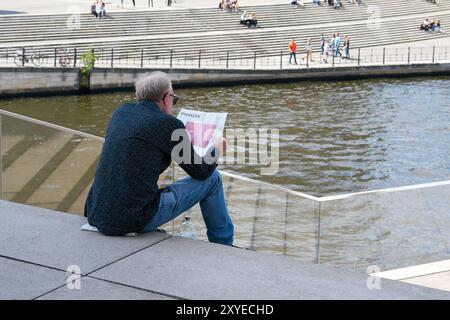 Un uomo siede su un gradino nel quartiere governativo di Berlino e legge la sezione finanziaria di un giornale Foto Stock