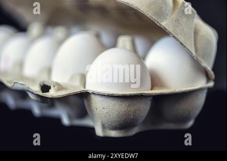 10 uova di pollo in un cartone da trasporto su sfondo nero Foto Stock