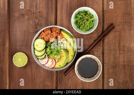 Una foto aerea di poke, tradizionale Hawaiiano pesce crudo insalata, con una piastra di wakame, mare vegetale, con bacchette, salsa, tigli e spazio di copia Foto Stock