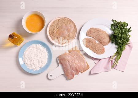 Fare schnitzel. Fette di carne con briciole di pane e ingredienti su un tavolo di legno bianco, distesa piatta Foto Stock