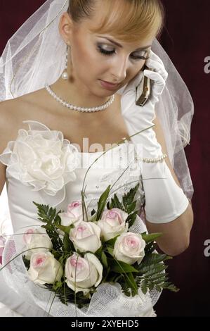 Giovane sposa in un abito da sposa con fiori che parlano al cellulare Foto Stock