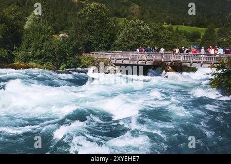 Norvegia, Olden, 1 agosto 2018: Persone al ponte e fiume d'acqua turchese dal ghiacciaio nelle montagne norvegesi, Europa Foto Stock