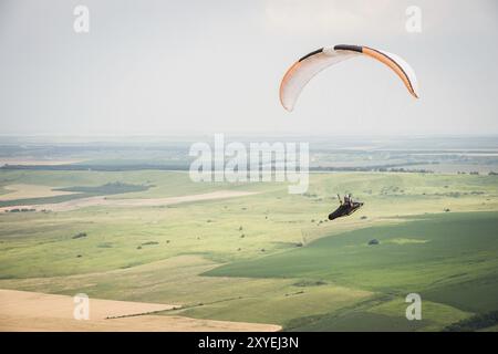 Parapendio bianco arancio con parapendio in bozzolo sullo sfondo di campi del cielo e nuvole. Parapendio Sport Foto Stock