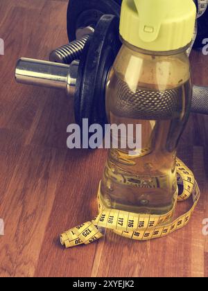 Acqua fredda e nastro di misurazione con manubri su un pavimento di legno Foto Stock