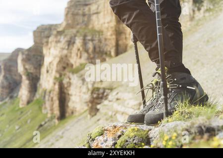 Primo piano di gambe femminili in stivali da trekking con bastoni per il nordic walking sullo sfondo di rocce e lontane terre caucasiche Foto Stock