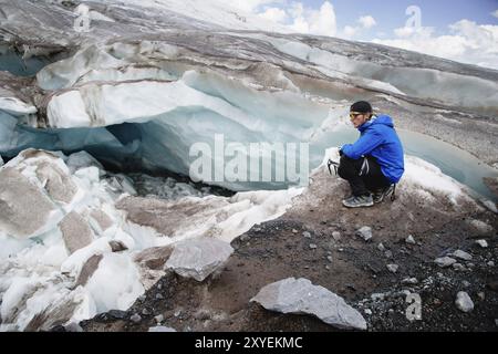 Il viaggiatore in una cuffia e gli occhiali da sole è seduto nelle montagne innevate sul ghiacciaio. Viaggiatori in un ambiente naturale Foto Stock