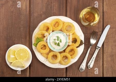 Anelli di totano con una maionese, limoni e un bicchiere di vino, girato dalla parte superiore al buio su un rustico sfondo di legno con spazio di copia Foto Stock