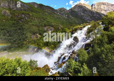 La cascata e rainbow sul modo di Briksdal o ghiacciaio Briksdalsbreen in Olden, Norvegia e montagne verdi Foto Stock