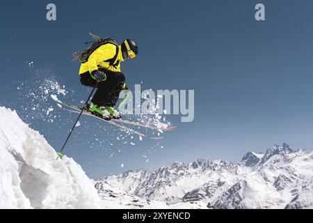 Uno sciatore con attrezzatura sportiva completa salta nel precipizio dalla cima del ghiacciaio sullo sfondo del cielo blu e della neve caucasica Foto Stock