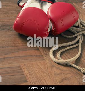 Red guantoni da pugilato e corda da salto su un rustico pavimento in legno in una palestra, sport o il concetto di assertività Foto Stock