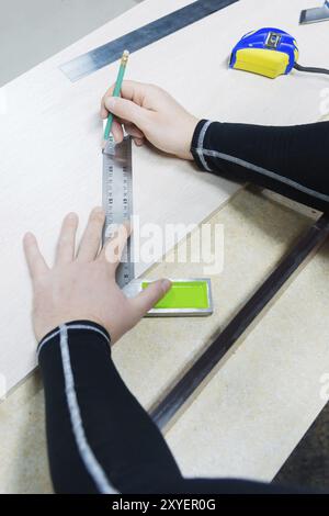 Primo piano Carpentry, mans Hand con metro a nastro per misurare la tavola di legno e contrassegnarla con una matita. Vista dall'alto Foto Stock