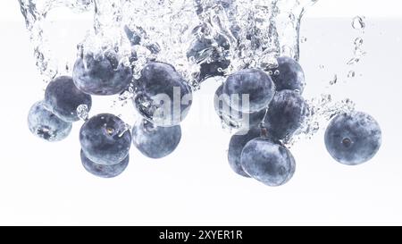 Un mucchio di mirtilli dall'aspetto delizioso che spruzzano sulla superficie dell'acqua e affondano. Isolata su sfondo bianco, scatta fotografie di cibo. Primo piano macro Foto Stock