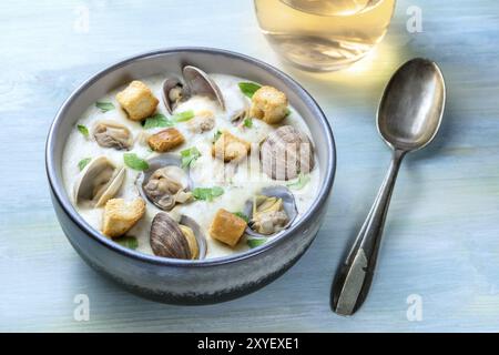 Clam Chowder, decorate con prezzemolo fresco e crostini, su uno sfondo blu con un bicchiere di vino bianco e un cucchiaio Foto Stock